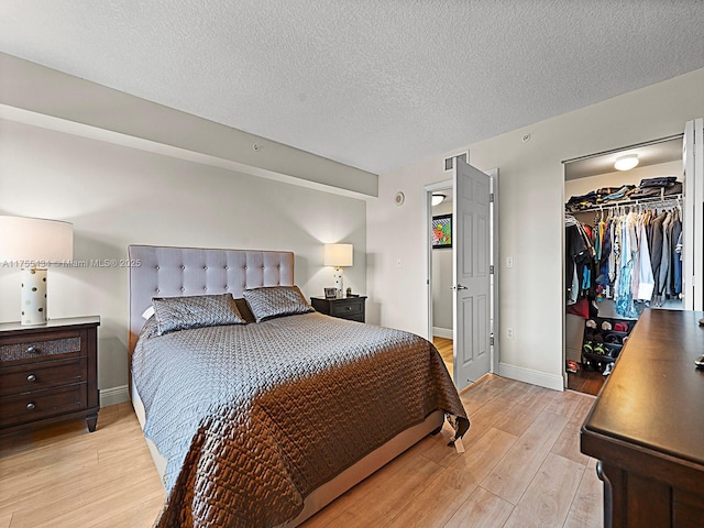 bedroom with visible vents, light wood-style flooring, a spacious closet, a textured ceiling, and baseboards