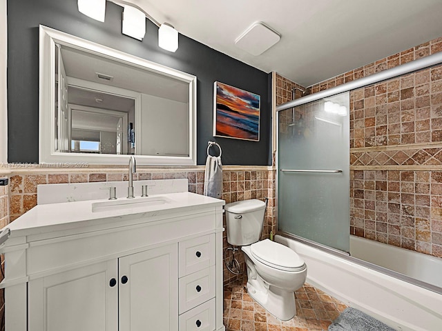 full bath featuring toilet, a wainscoted wall, combined bath / shower with glass door, vanity, and tile walls