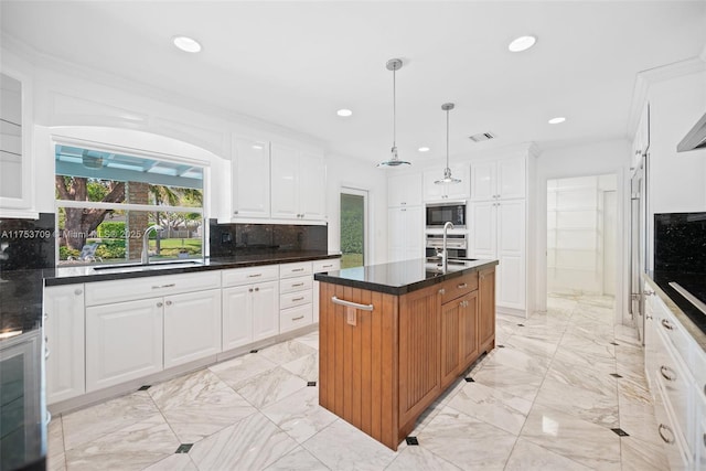 kitchen featuring marble finish floor, backsplash, white cabinetry, an island with sink, and built in microwave