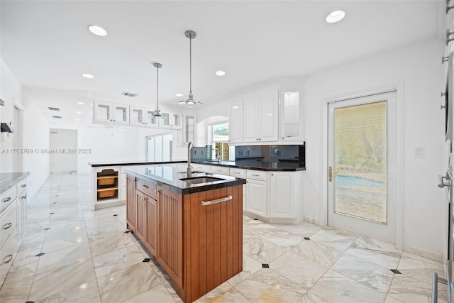 kitchen featuring a sink, white cabinets, marble finish floor, an island with sink, and glass insert cabinets