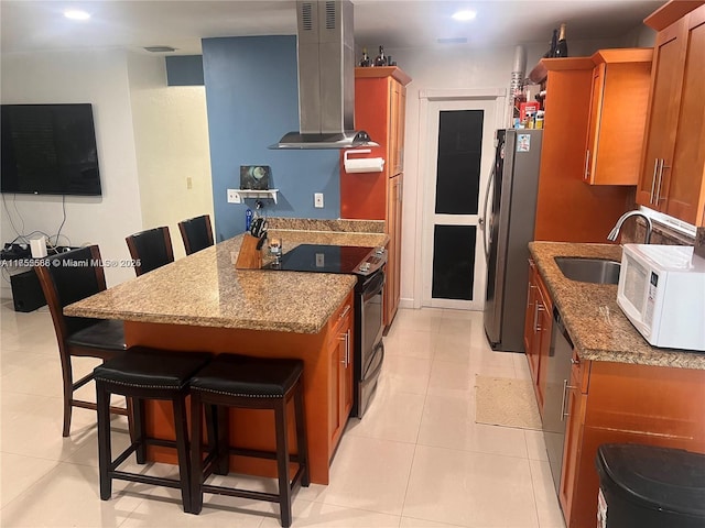 kitchen with brown cabinets, a breakfast bar area, stainless steel appliances, a sink, and wall chimney exhaust hood