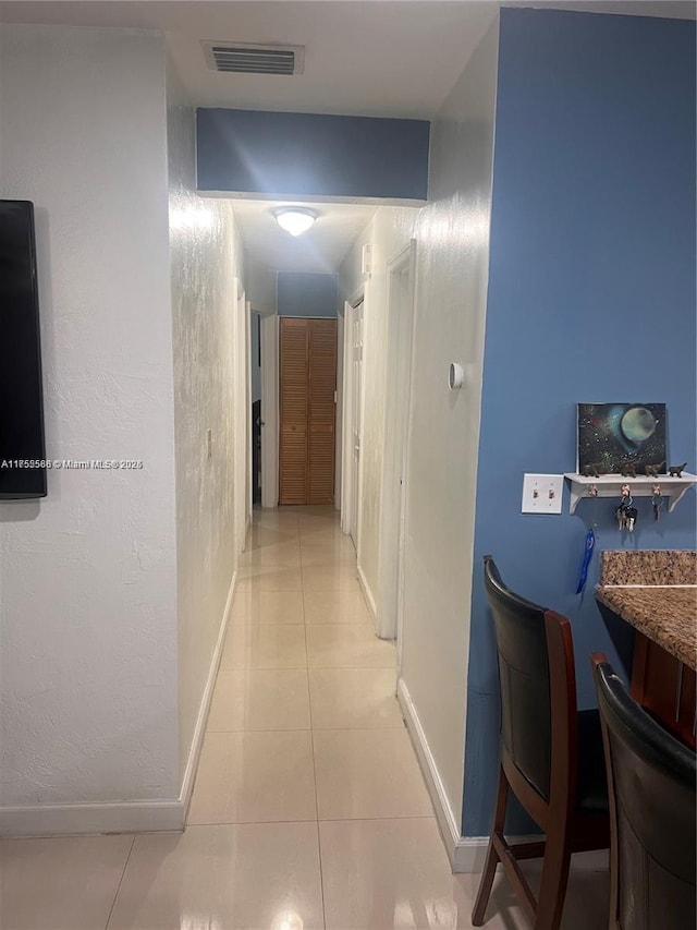 hall featuring visible vents, baseboards, and light tile patterned flooring