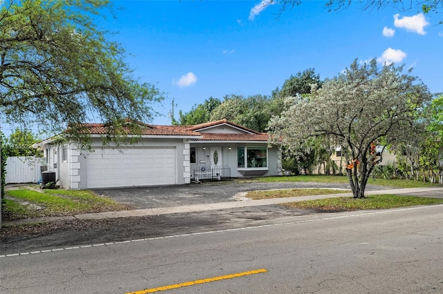 ranch-style house featuring aphalt driveway, a garage, fence, a tile roof, and stucco siding