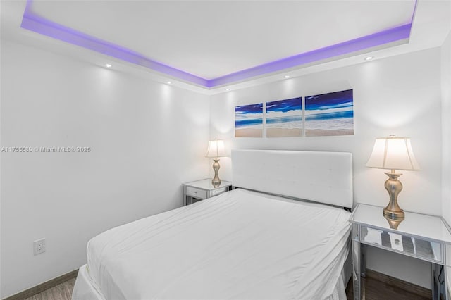 bedroom featuring baseboards, a raised ceiling, and wood finished floors