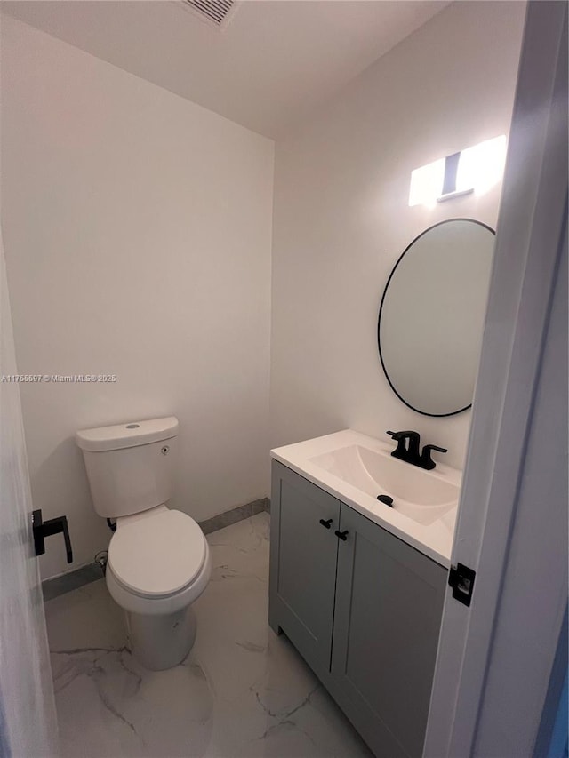 half bathroom with marble finish floor, toilet, vanity, and baseboards