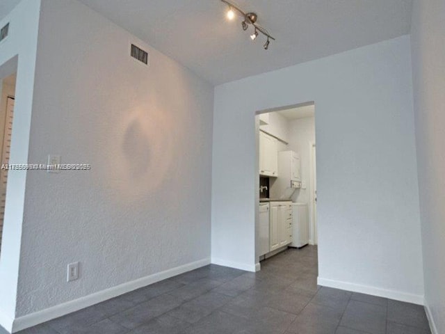 empty room with track lighting, visible vents, and baseboards