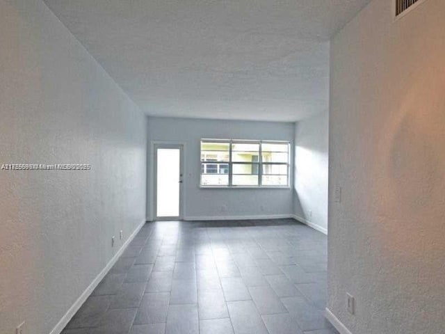 empty room featuring a textured wall, visible vents, and baseboards