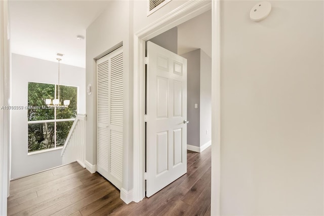 corridor featuring dark wood-style floors, baseboards, visible vents, and an inviting chandelier