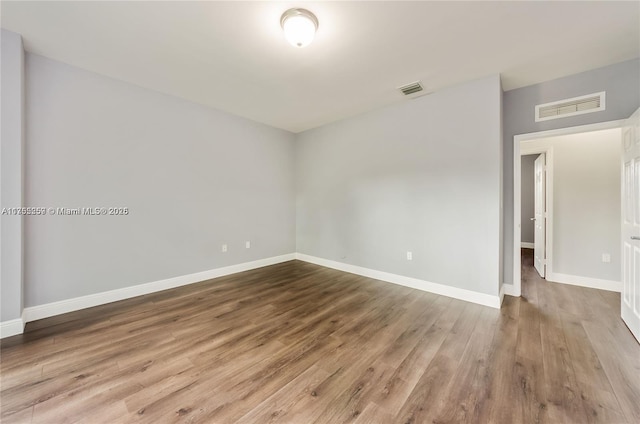 unfurnished room with baseboards, visible vents, and wood finished floors