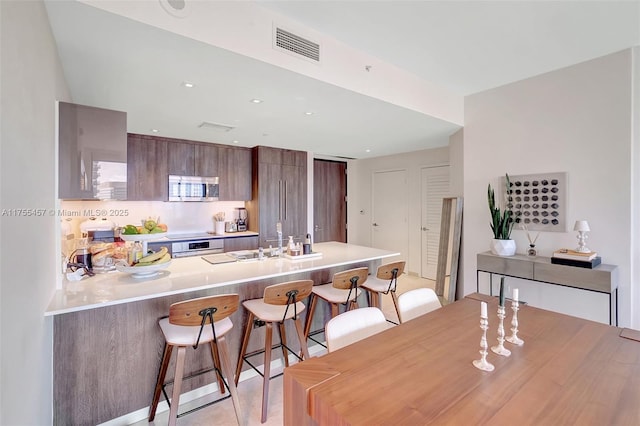 kitchen with visible vents, modern cabinets, stainless steel microwave, a peninsula, and a kitchen bar