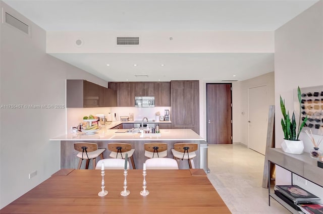 kitchen with a breakfast bar area, a peninsula, visible vents, light countertops, and modern cabinets