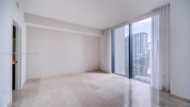 unfurnished room with a healthy amount of sunlight, a view of city, visible vents, and a wall of windows