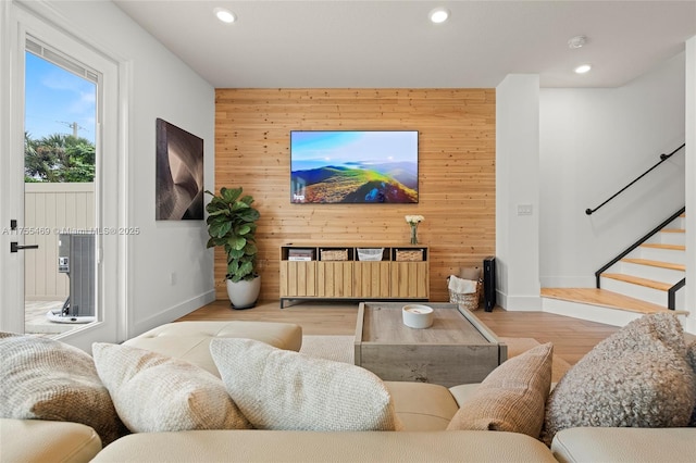 living room with stairs, an accent wall, wood finished floors, and wooden walls