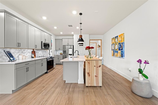 kitchen featuring visible vents, appliances with stainless steel finishes, gray cabinets, light wood finished floors, and tasteful backsplash