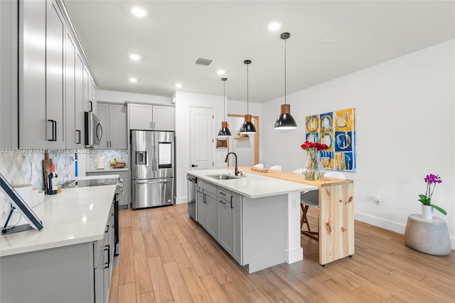 kitchen with light wood-style flooring, gray cabinetry, a sink, appliances with stainless steel finishes, and backsplash