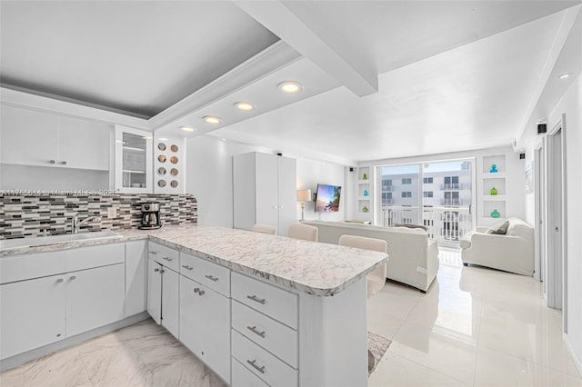 kitchen with open floor plan, a peninsula, a sink, light countertops, and backsplash