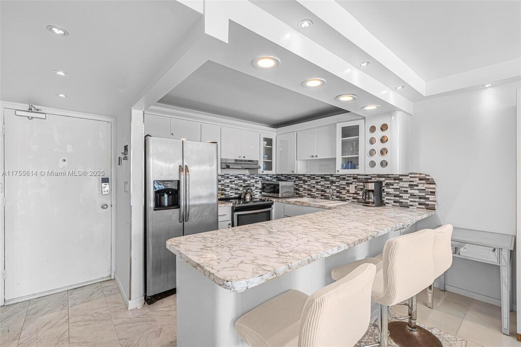 kitchen with tasteful backsplash, glass insert cabinets, light countertops, appliances with stainless steel finishes, and a peninsula