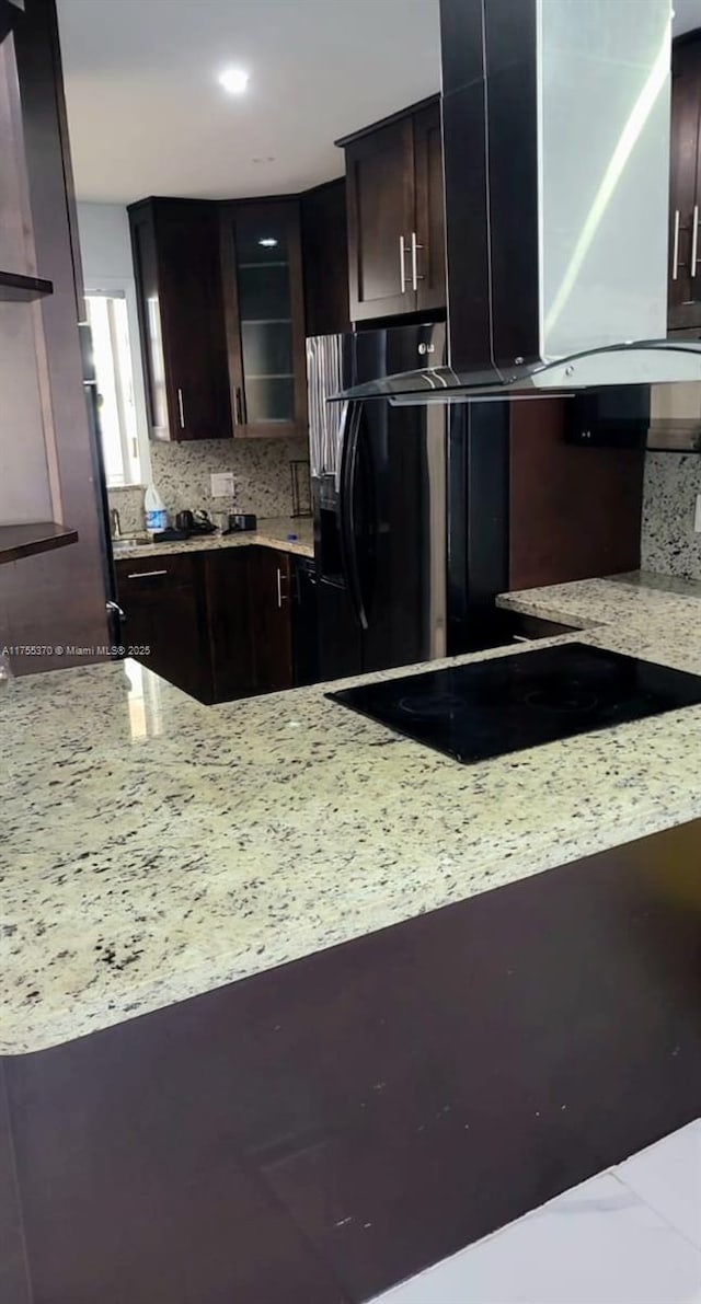 kitchen featuring dark brown cabinets, glass insert cabinets, light stone countertops, decorative backsplash, and black electric cooktop