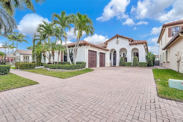 mediterranean / spanish-style house with a tile roof, an attached garage, decorative driveway, a front lawn, and stucco siding