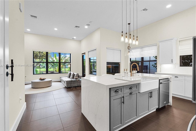 kitchen featuring visible vents, open floor plan, light stone countertops, a kitchen island with sink, and a sink