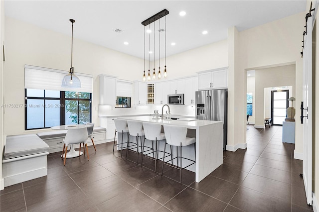 kitchen featuring a kitchen breakfast bar, a kitchen island with sink, a high ceiling, stainless steel appliances, and light countertops