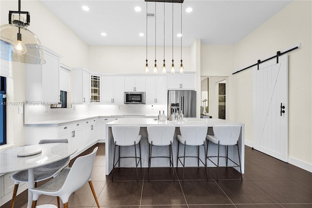 kitchen featuring a barn door, glass insert cabinets, appliances with stainless steel finishes, a breakfast bar, and a kitchen island with sink