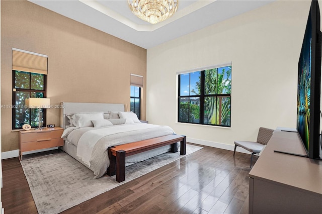 bedroom featuring dark wood-type flooring, a tray ceiling, a notable chandelier, and baseboards