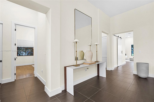 corridor with dark tile patterned floors, a barn door, and baseboards