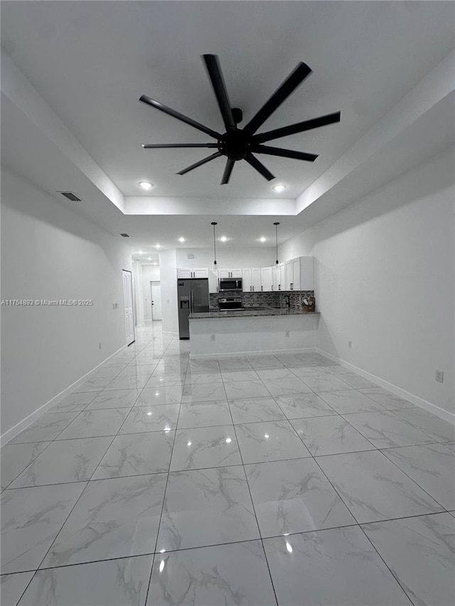 unfurnished living room with recessed lighting, a raised ceiling, marble finish floor, and baseboards