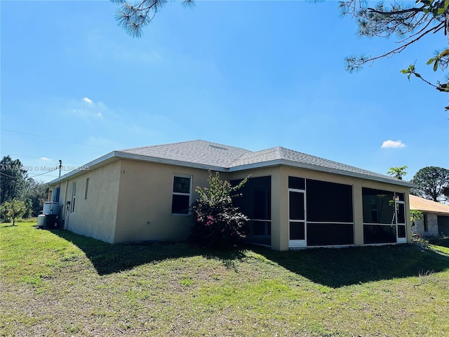 back of property with stucco siding, roof with shingles, a sunroom, and a yard