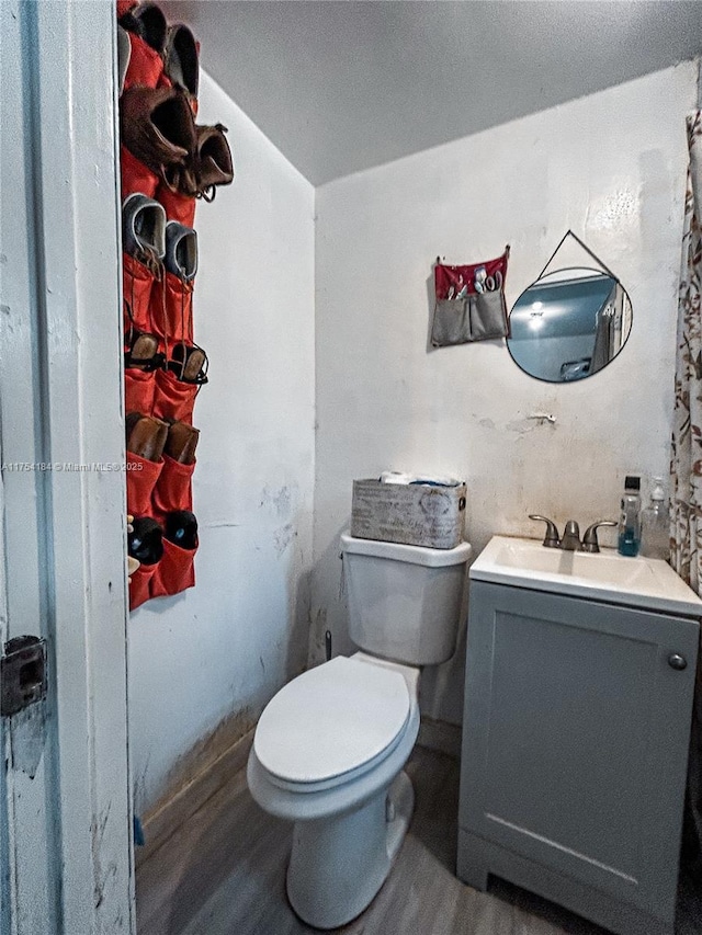 half bathroom with toilet, wood finished floors, and vanity