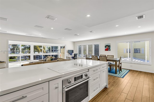 kitchen featuring light wood-style flooring, oven, visible vents, white cabinets, and white electric stovetop