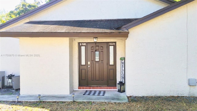 doorway to property featuring a shingled roof and stucco siding