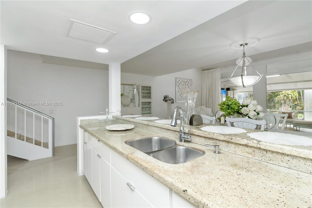 kitchen with decorative light fixtures, visible vents, white cabinets, a sink, and light stone countertops