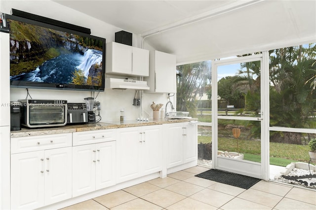 kitchen featuring light stone countertops, white cabinets, under cabinet range hood, and light tile patterned floors