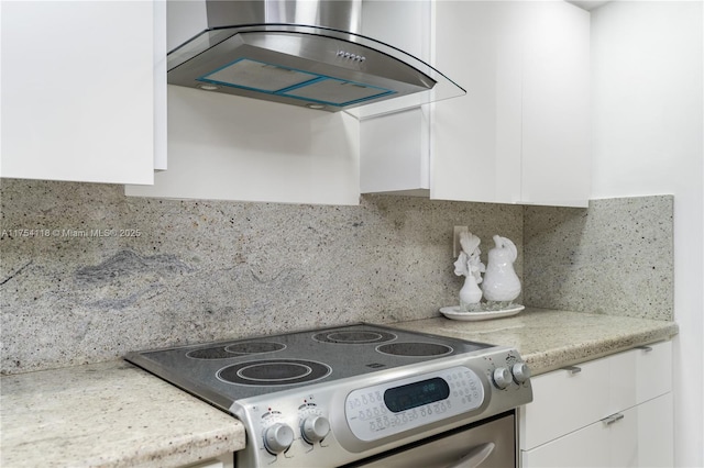 kitchen with wall chimney range hood, tasteful backsplash, white cabinetry, and range with electric stovetop