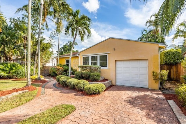 view of front of home with stucco siding, a garage, driveway, and fence