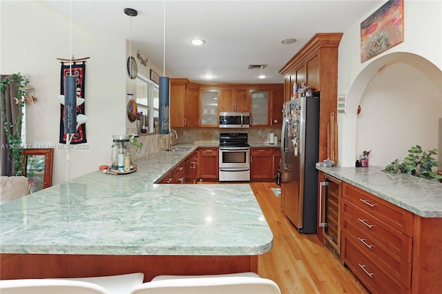 kitchen featuring beverage cooler, a sink, stainless steel appliances, a peninsula, and brown cabinetry