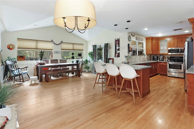 kitchen with brown cabinets, light wood-style flooring, appliances with stainless steel finishes, a breakfast bar area, and a peninsula