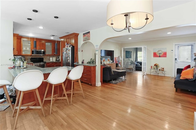 kitchen with brown cabinetry, a peninsula, stainless steel appliances, glass insert cabinets, and light wood-type flooring