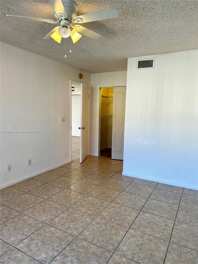 spare room with a textured ceiling, ceiling fan, light tile patterned flooring, visible vents, and baseboards