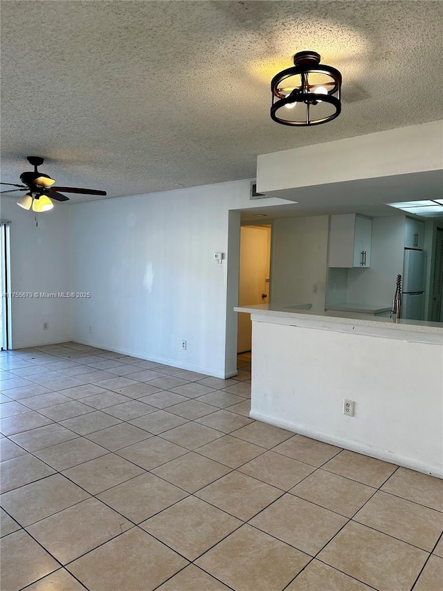 empty room with light tile patterned floors, ceiling fan, and a textured ceiling