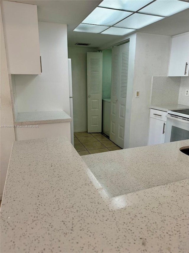 kitchen with light tile patterned floors, light stone counters, white appliances, visible vents, and white cabinetry