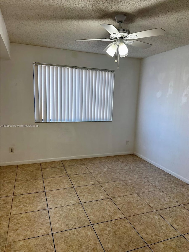 empty room with a ceiling fan, tile patterned flooring, baseboards, and a textured ceiling