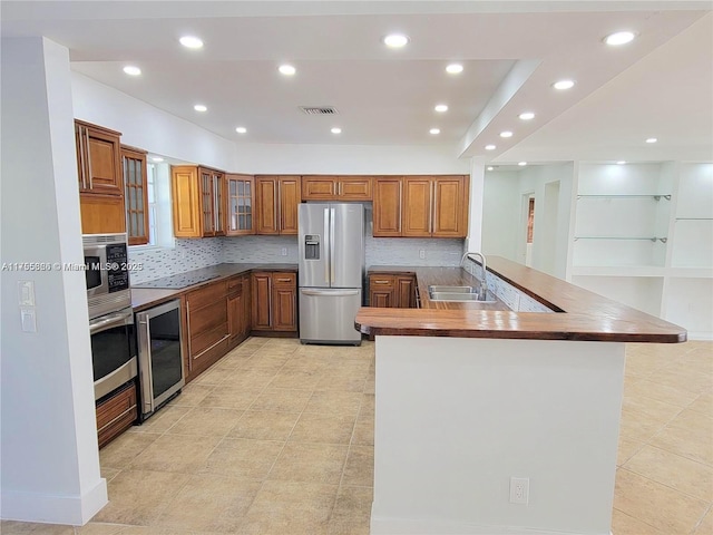 225 191st Ter, Sunny Isles Beach, FL 33160 - kitchen with appliances with stainless steel finishes, beverage cooler, brown cabinets, a peninsula, and decorative backsplash