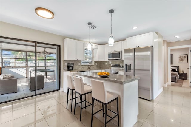 kitchen with backsplash, appliances with stainless steel finishes, white cabinets, a sink, and a kitchen bar