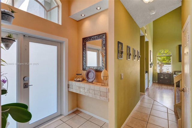 entrance foyer with light tile patterned floors, a textured ceiling, a towering ceiling, and baseboards