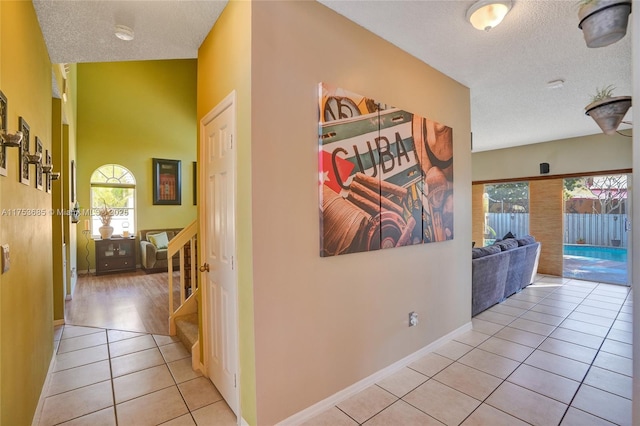 hall featuring a textured ceiling, stairway, baseboards, and tile patterned floors