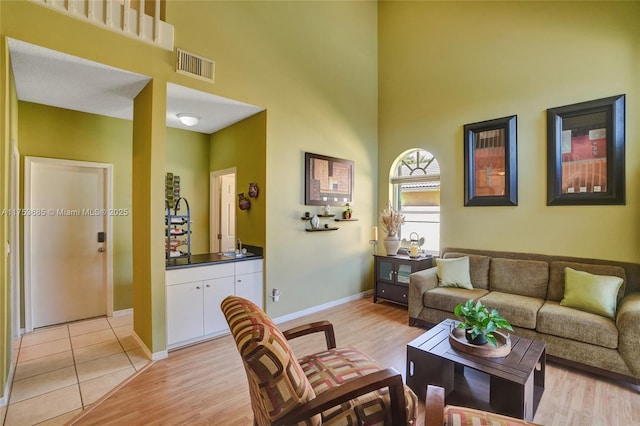 living area with light wood finished floors, a high ceiling, and visible vents