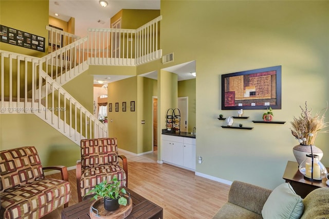 living room with stairs, light wood-type flooring, a towering ceiling, and baseboards